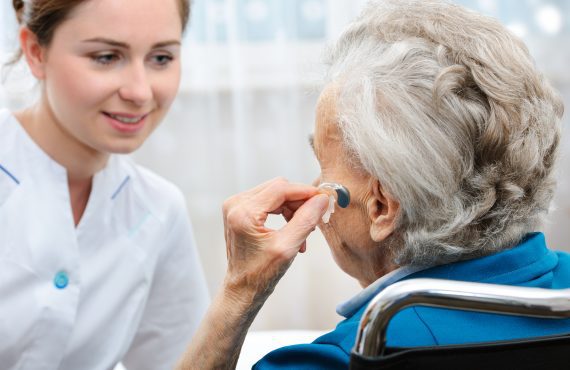 A senior woman with a hearing aid talking to a nurse.